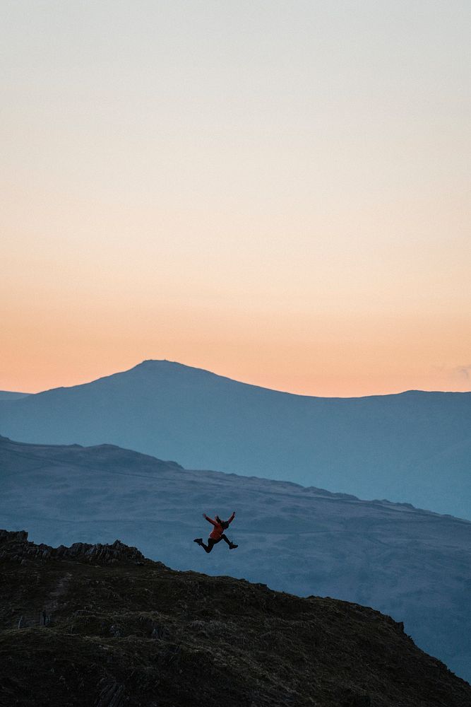 Woman jumping on a summit of Loughrigg Fell at Lake District in England