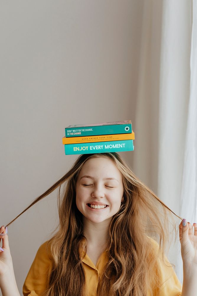 Cheerful blond girl balancing books on her head