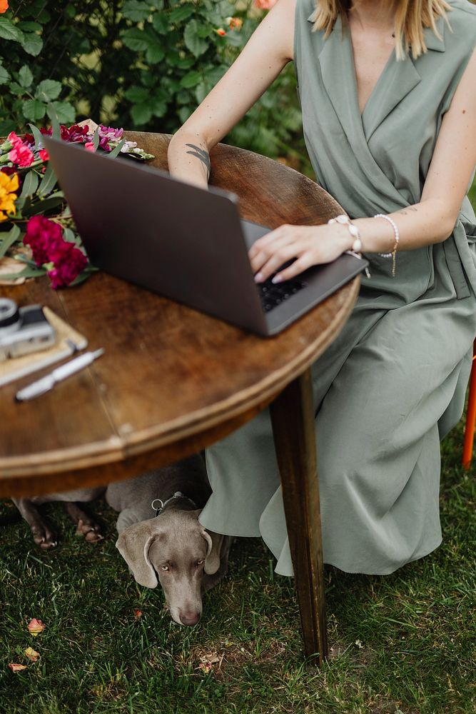 Woman with a laptop in the garden working with her dog