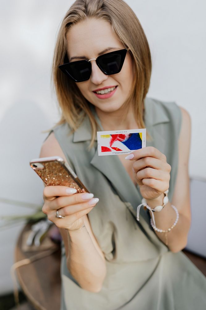 Friendly woman in sunglasses taking a photo of a business card with her smartphone