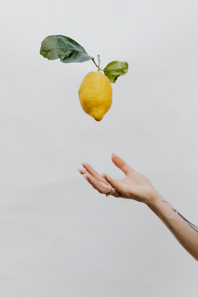Tattooed hand throwing a lemon up in a gray sky