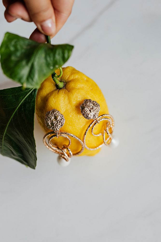 Hand holding a lemon with gold earrings on
