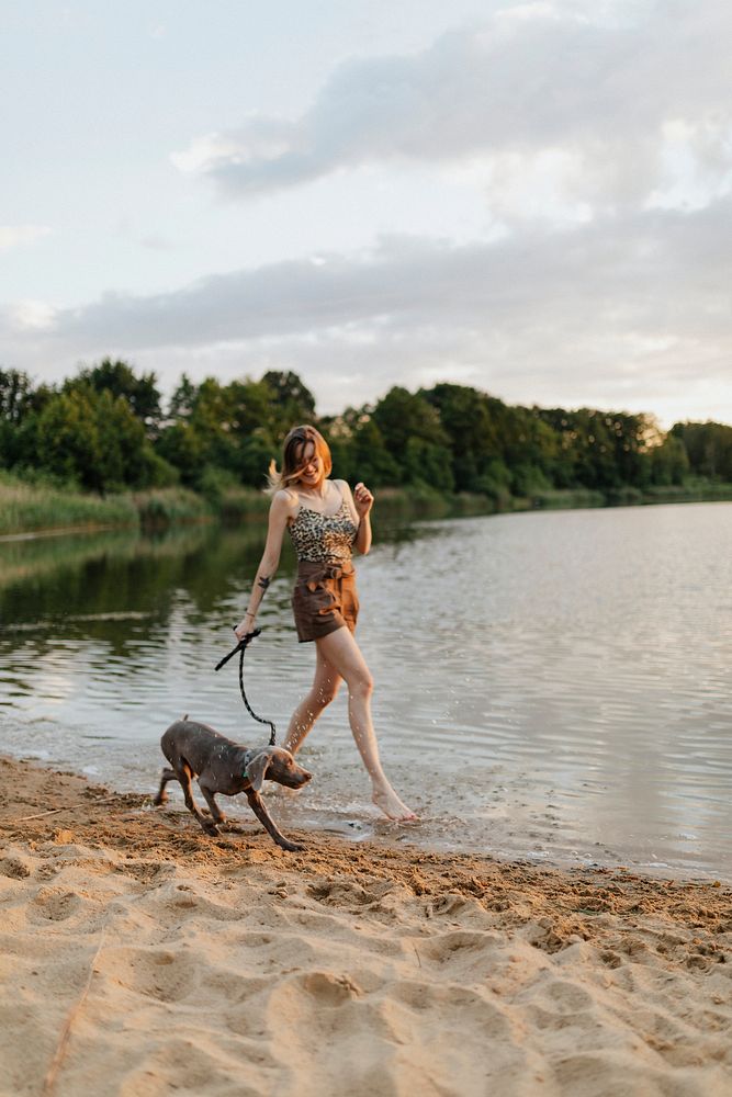 Cheerful woman walks with her Weimaraner dog by the lake