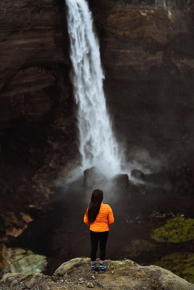 Woman in an orange jacket at the Haifoss waterfall, Iceland