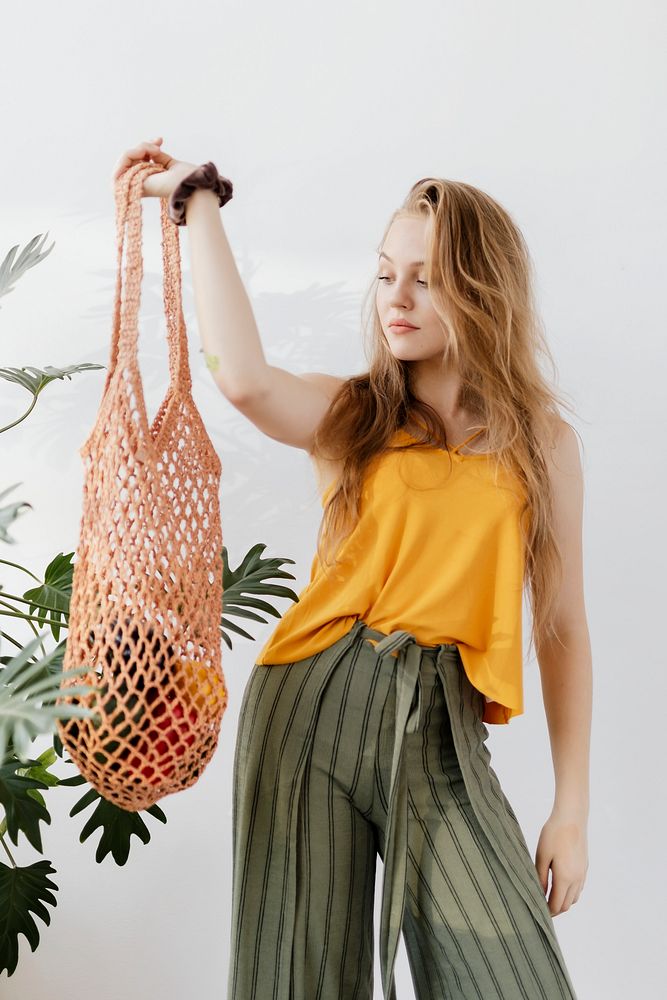 Blond girl holding a net bag with vegetables inside