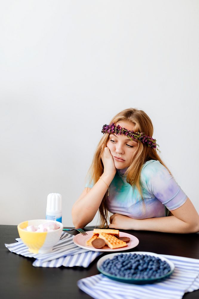Bored woman sitting by a plate with waffles 
