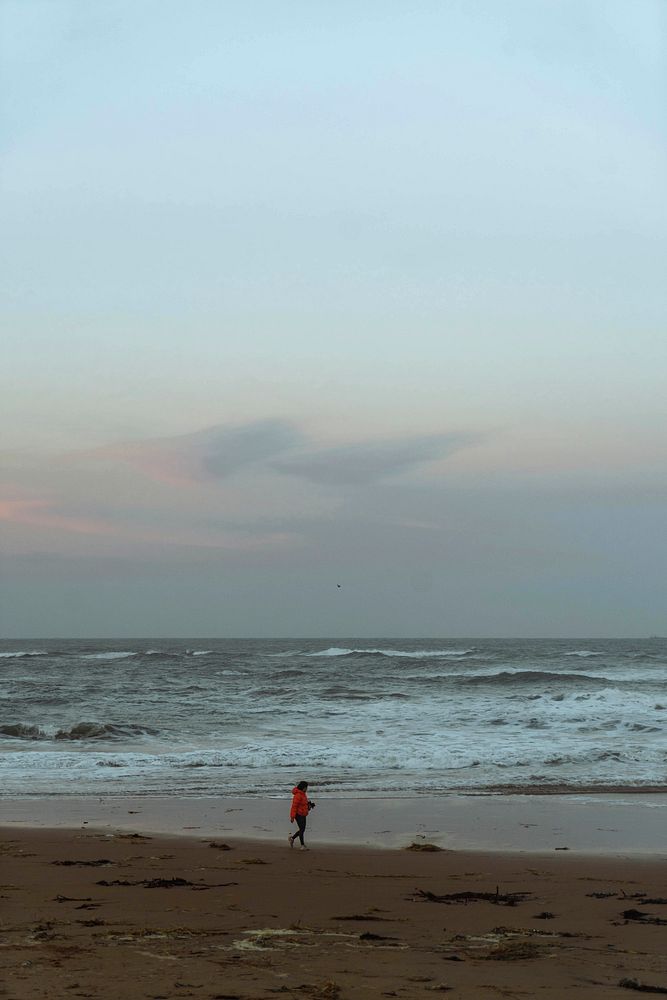 Woman walking along the coast during sunset, Scotland