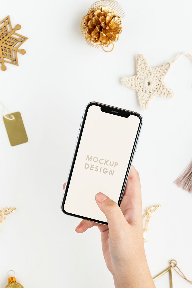 Woman holding her phone above gold Christmas ornaments mockup
