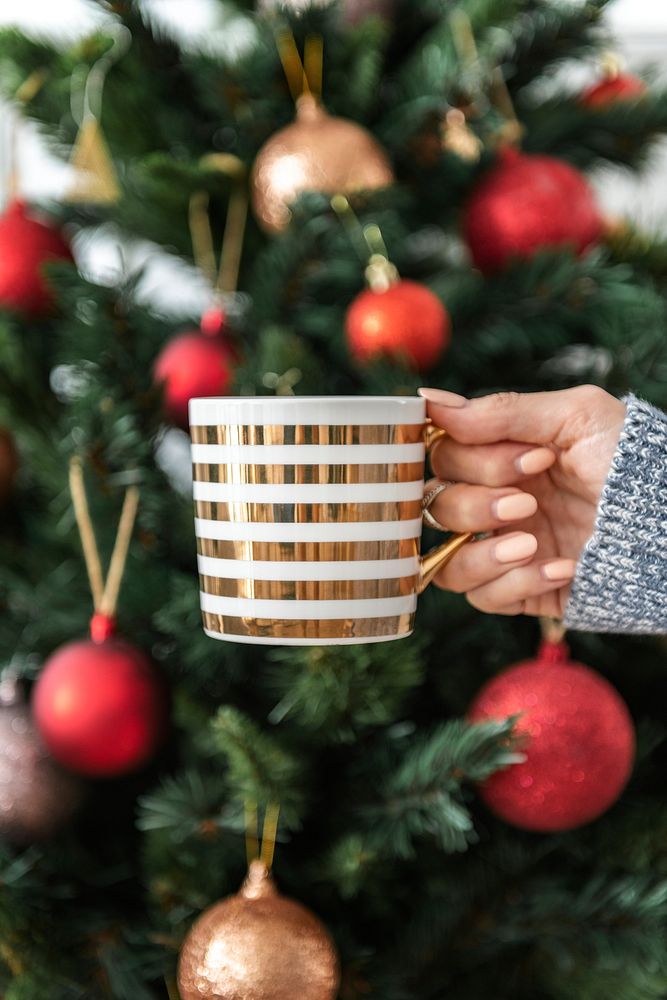 Woman holding a striped cup by Christmas tree