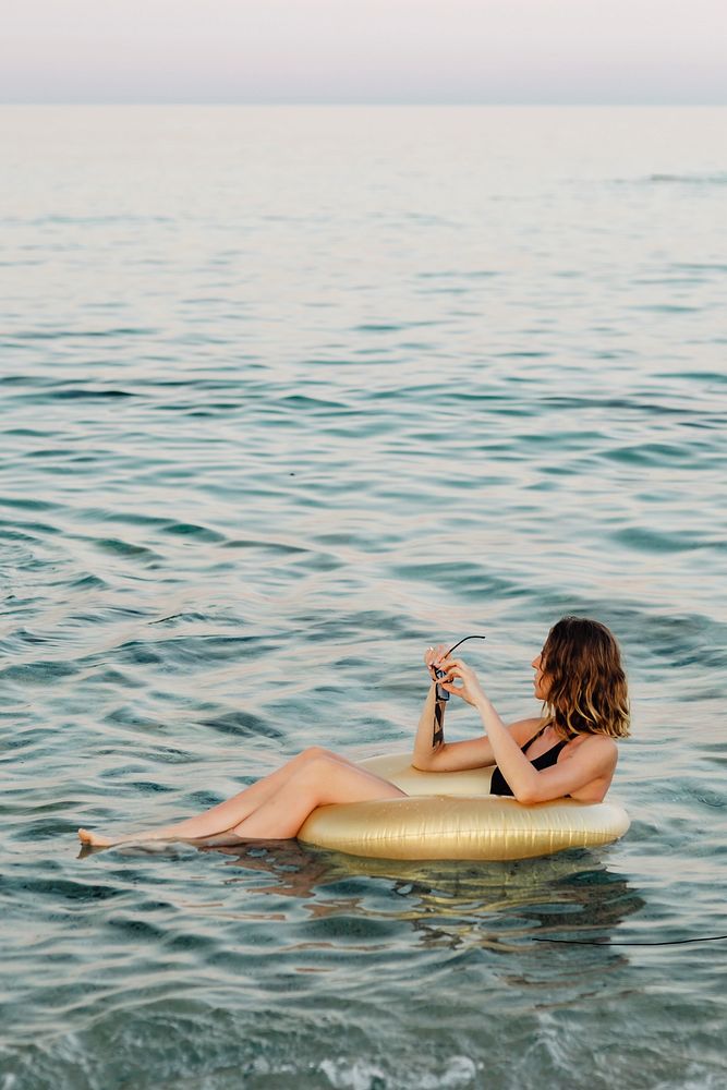 Girl sitting on a gold swim tube in the ocean