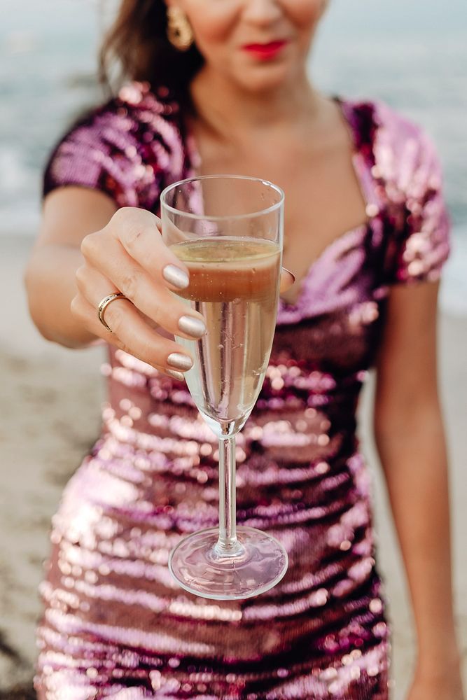 Woman in a pink dress having a glass of champagne at the beach