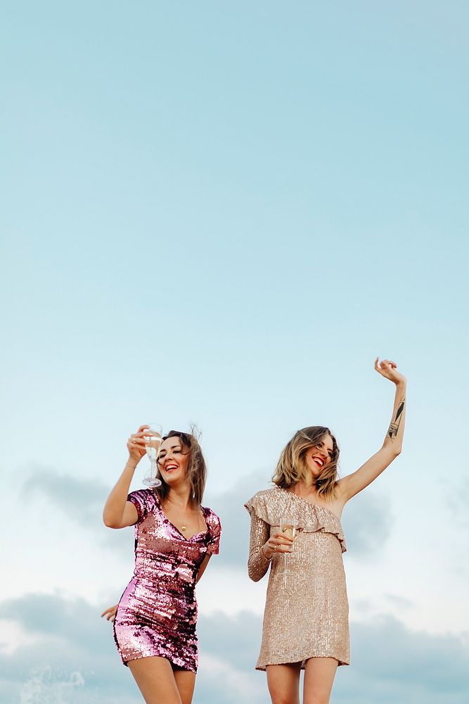 Women dancing with glasses of champagne at the beach