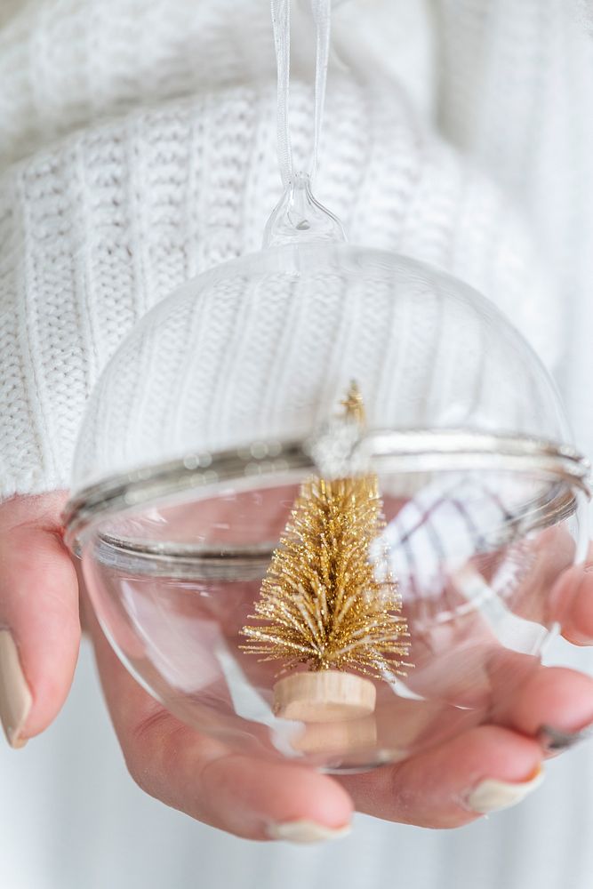 Woman holding a glass bauble with gold Christmas tree inside