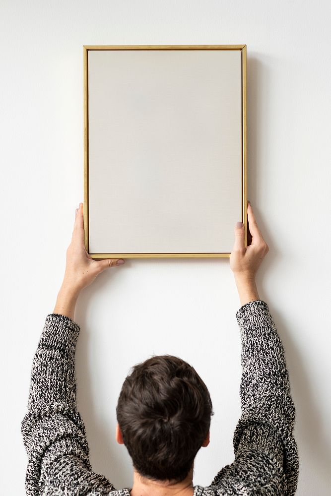 Woman in a black sweater hanging a wooden frame on a white wall mockup
