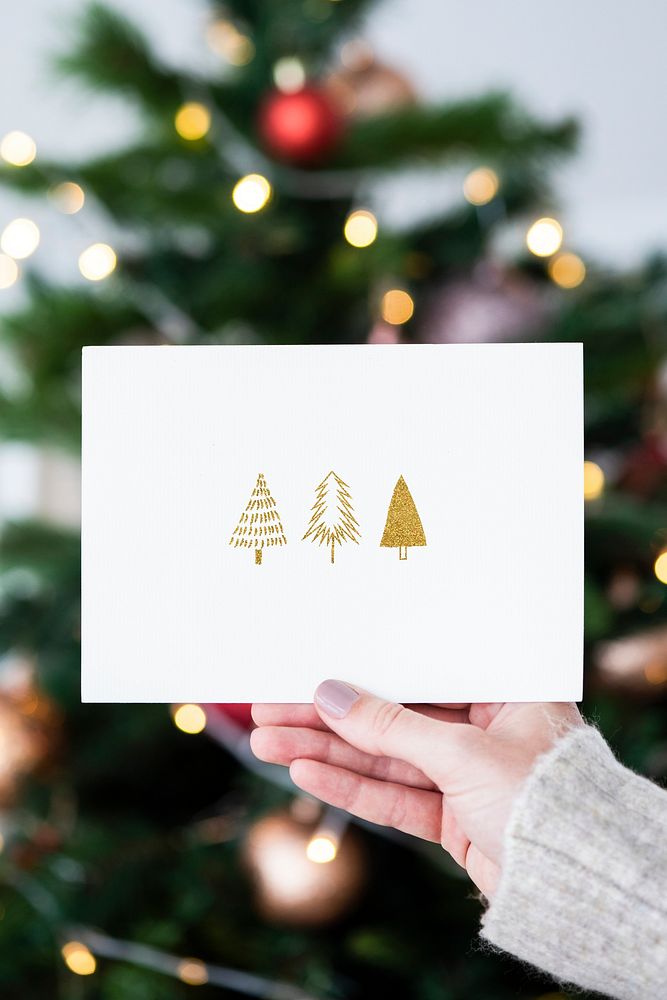 Woman holding a Christmas card in front of a Christmas tree
