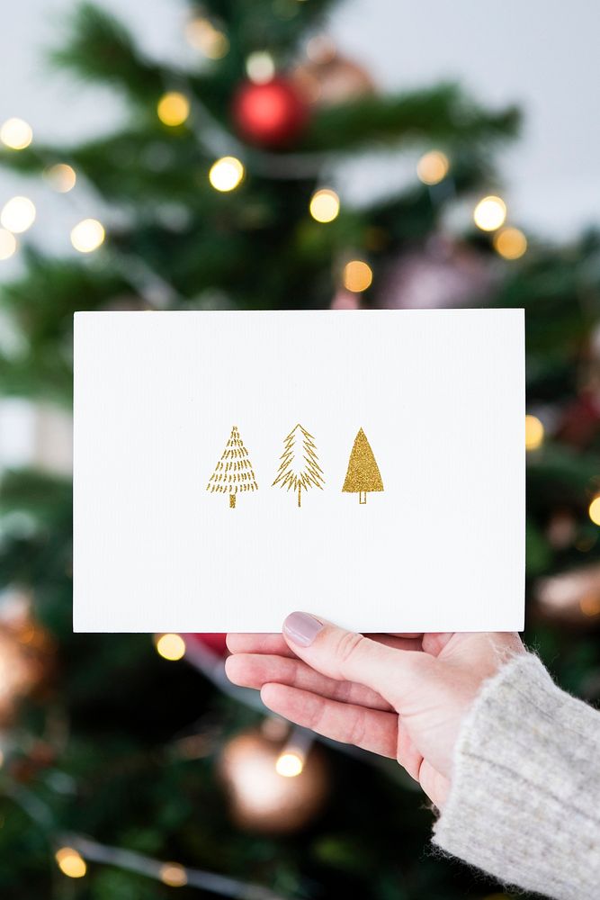 Woman holding a Christmas card in front of a Christmas tree mockup