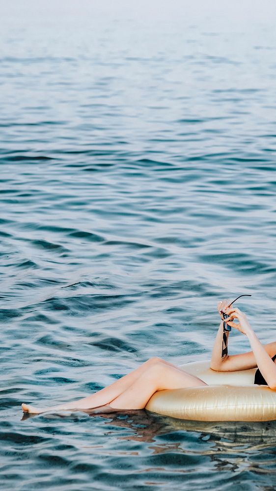 Girl sitting on a gold swim tube in the ocean mobile phone wallpaper