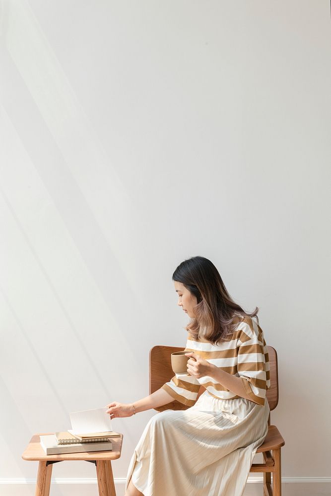 Asian woman drinking coffee while reading a book at home