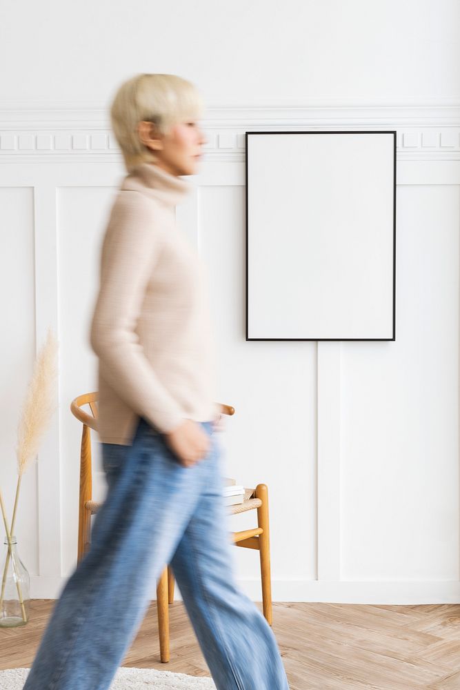 Woman walking past a black photo frame on a white wall mockup