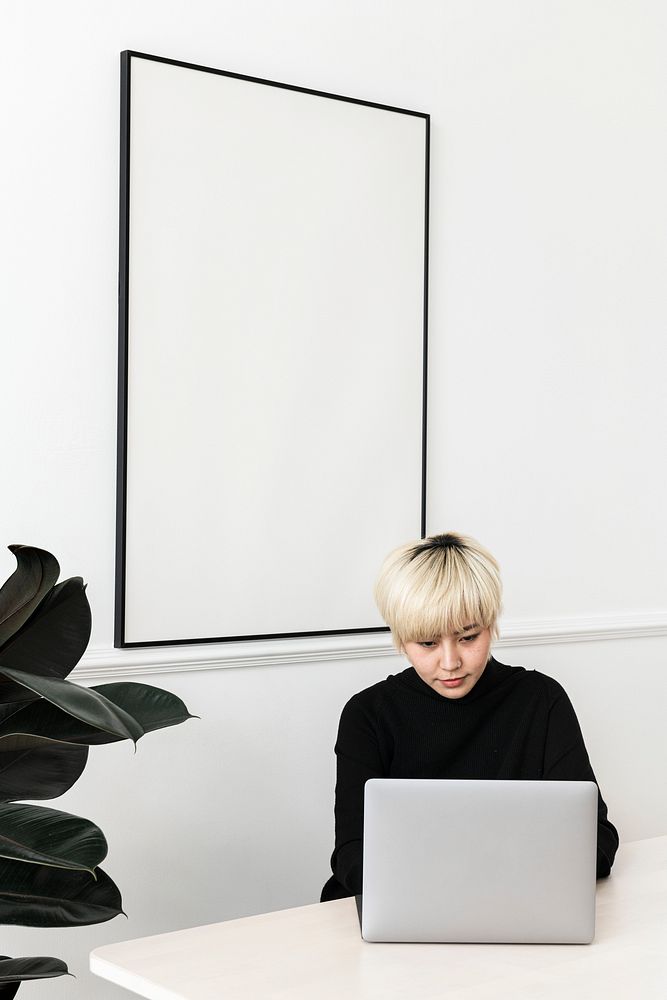 Woman working on her laptop with a blank frame hanging on a wall