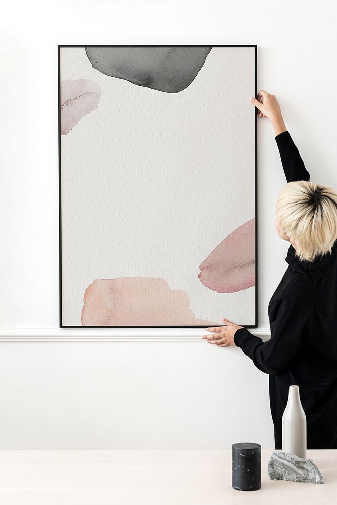 Blond haired Asian woman hanging a frame mockup on a white wall