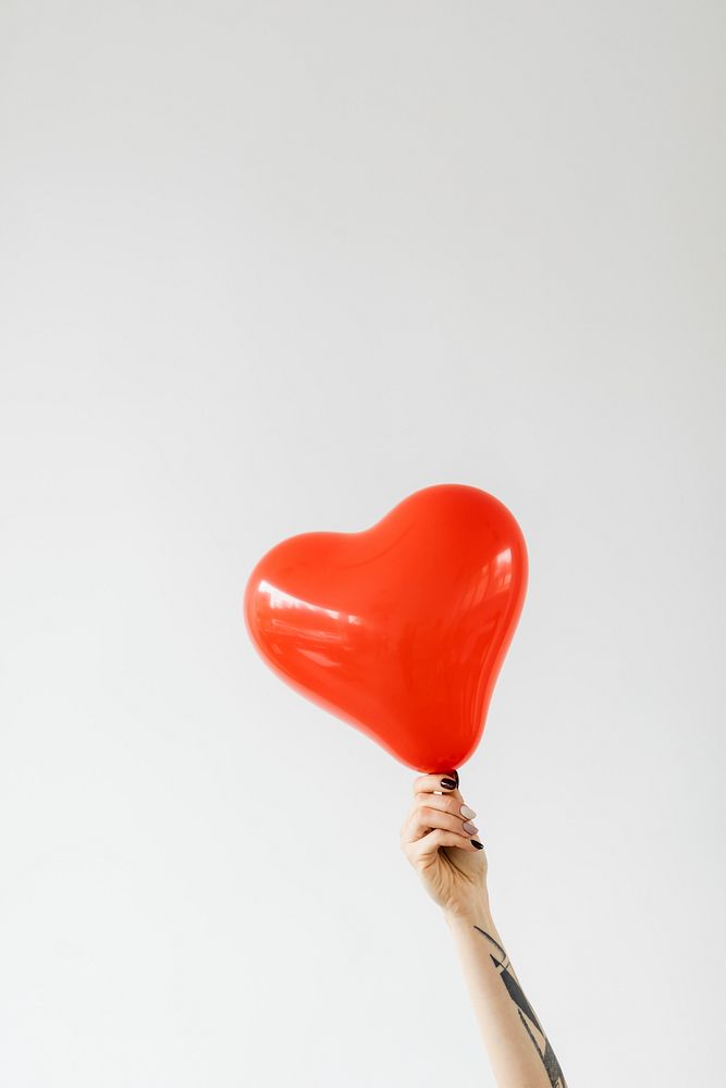Tattooed arm holding a red heart shape balloon