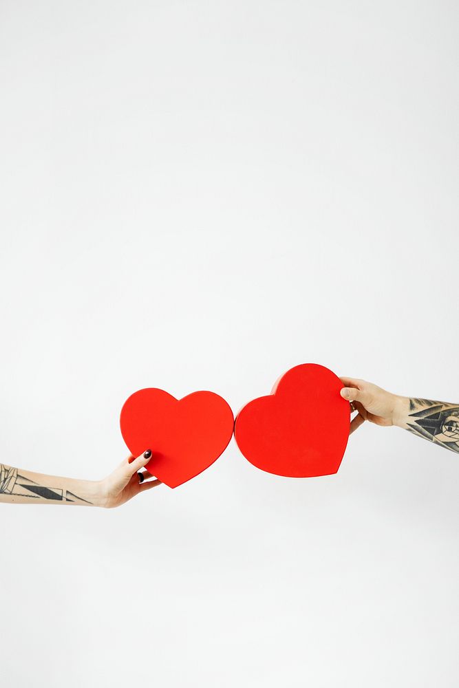 Tattooed hands holding red hearts 