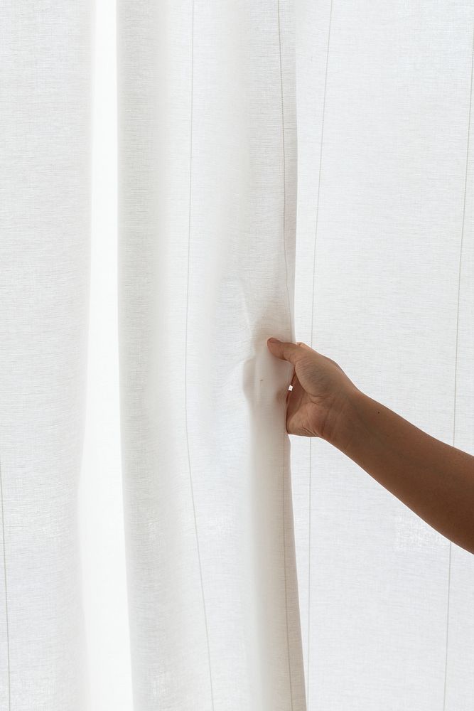 Hand opening a white curtain