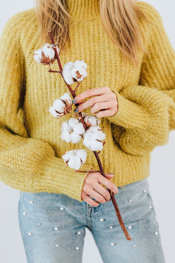 Woman in a yellow knitted sweater holding a cotton plant 