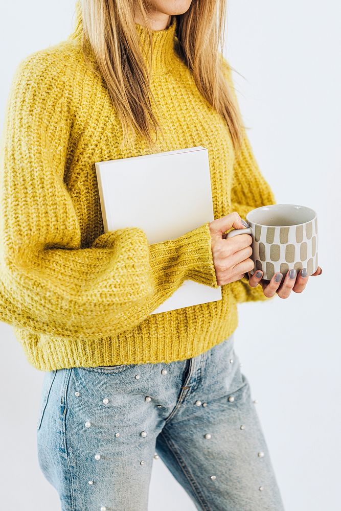 Woman wearing a cozy yellow sweater with a notebook and a cup of warm tea 