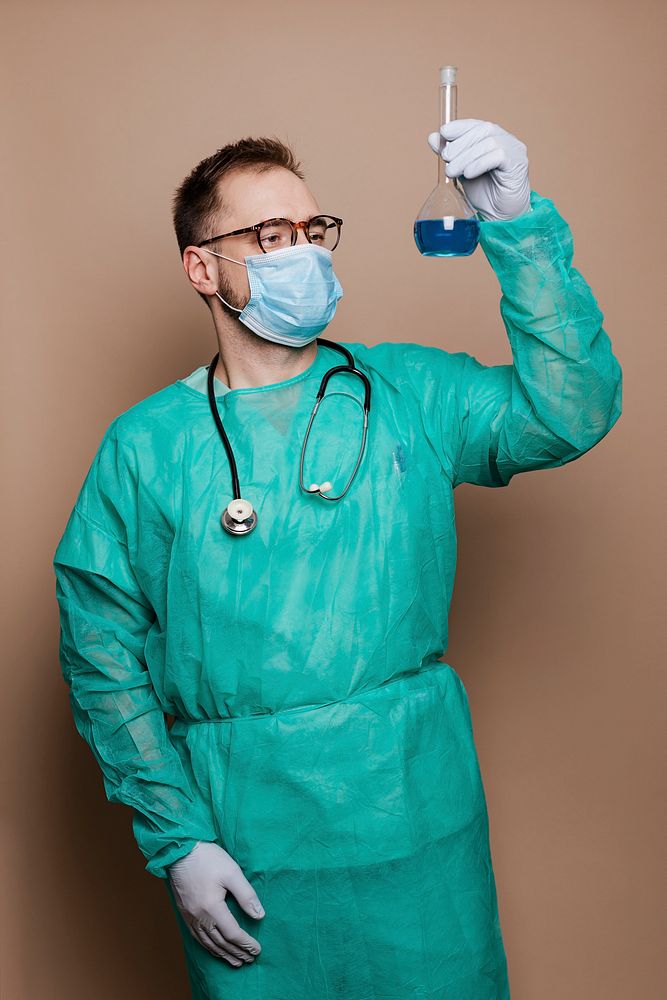 Microbiologist in a green gown holding a volumetric flask