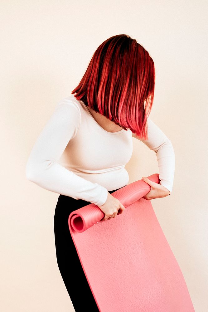 Woman in long sleeve top rolling pink yoga mat studio shot