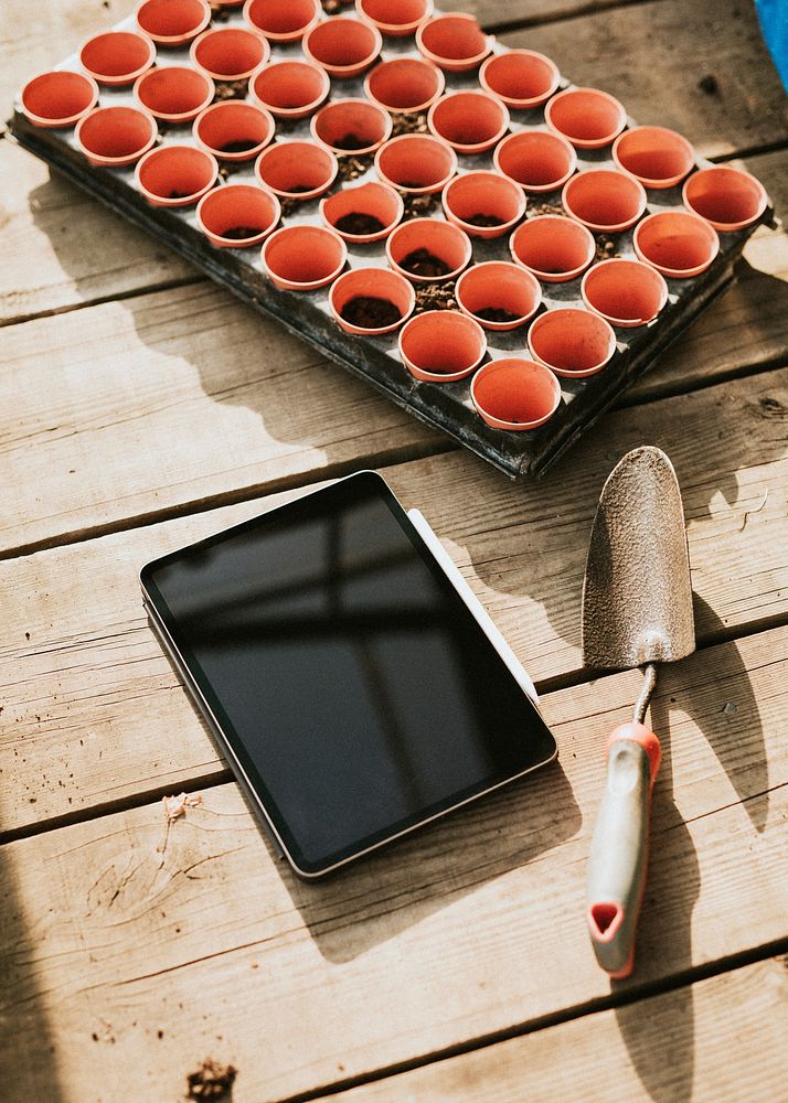 Black tablet by a gardening trowel on a wooden table