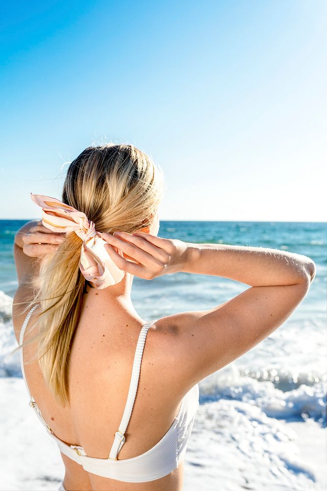 Blonde woman tying a ponytail at the beach back view