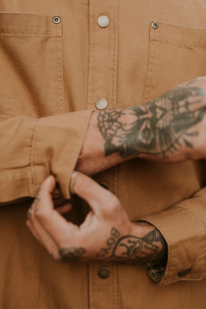 Tattooed man buttoning his brown shirt closeup