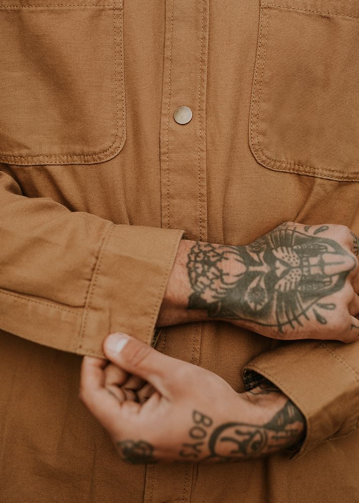 Tattooed man buttoning his brown shirt closeup