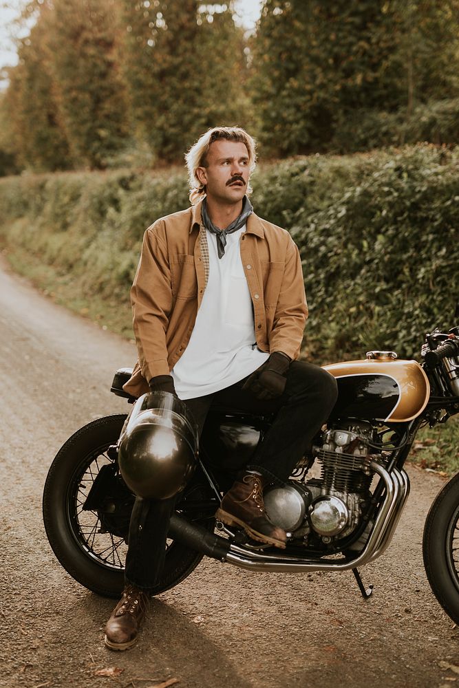 Handsome hipster man sitting on a retro motorcycle in the countryside