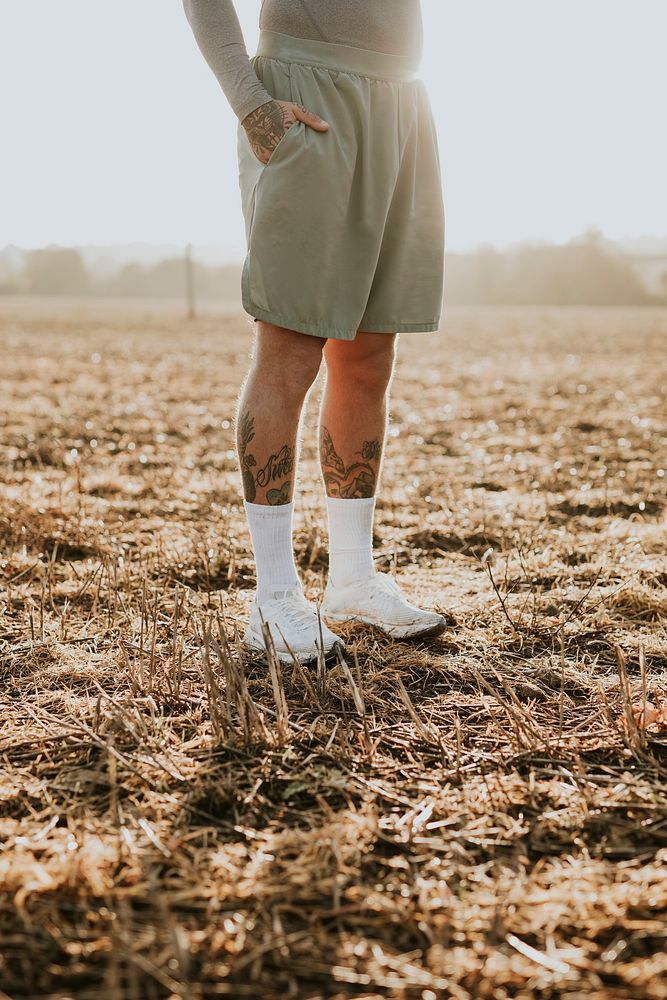 Tattooed man in running shorts standing in countryside at sunset