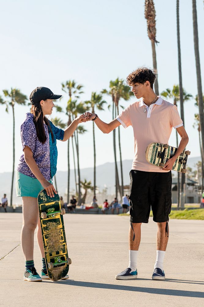 Teen friends fist bump, skaters at Venice Beach, Los Angeles