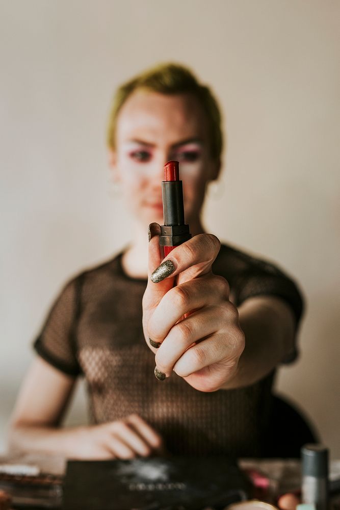 Non-binary beauty blogger holding red lipstick