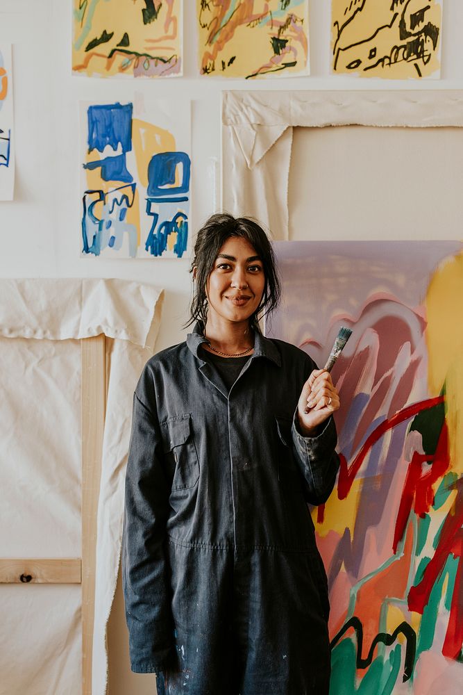 Woman artist holding a paint brush in front of her artworks