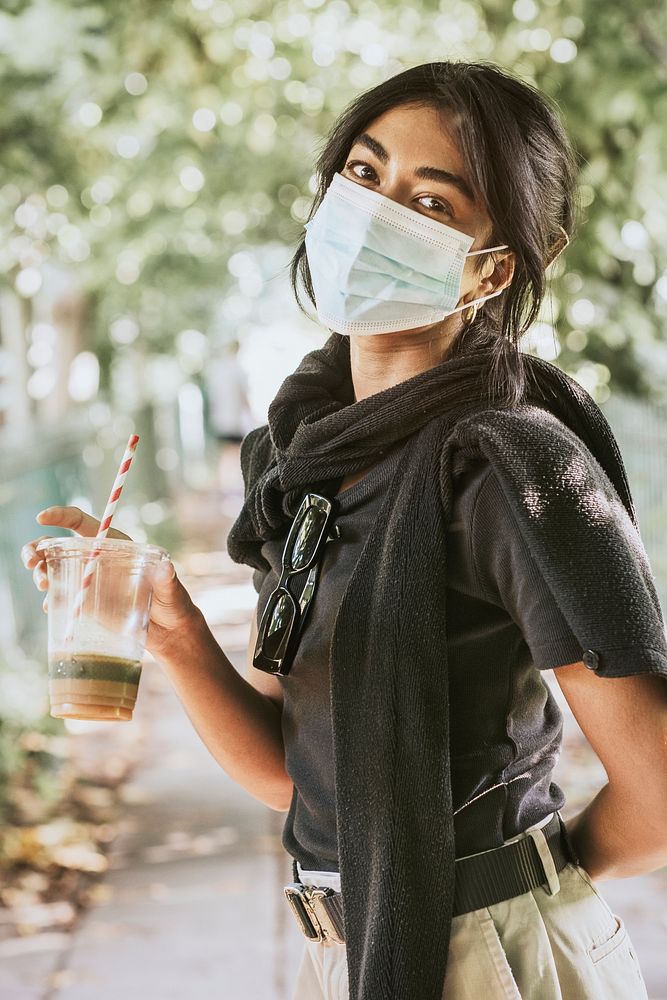 Woman wearing surgical mask carrying a cup of coffee 