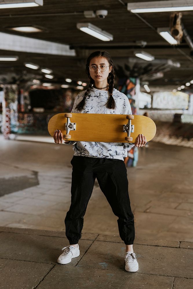 Cool woman standing in skate park with yellow skateboard