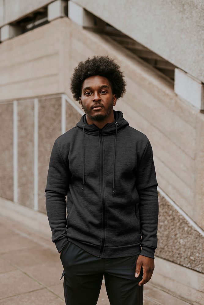 Man in dark gray zip up hoodie standing by a staircase