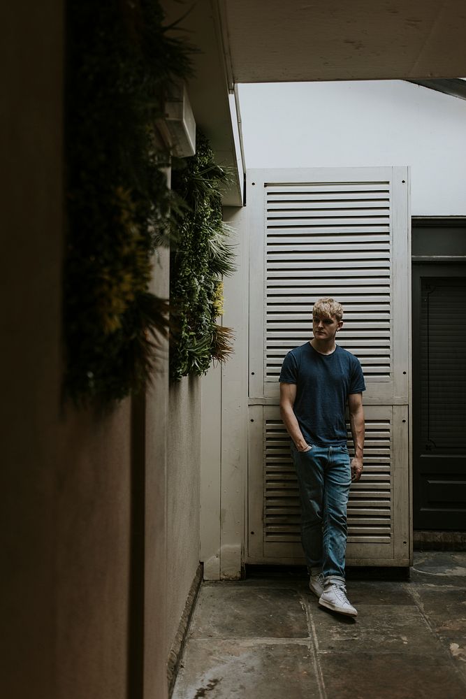 Blond man in blue t-shirt, in front of white door