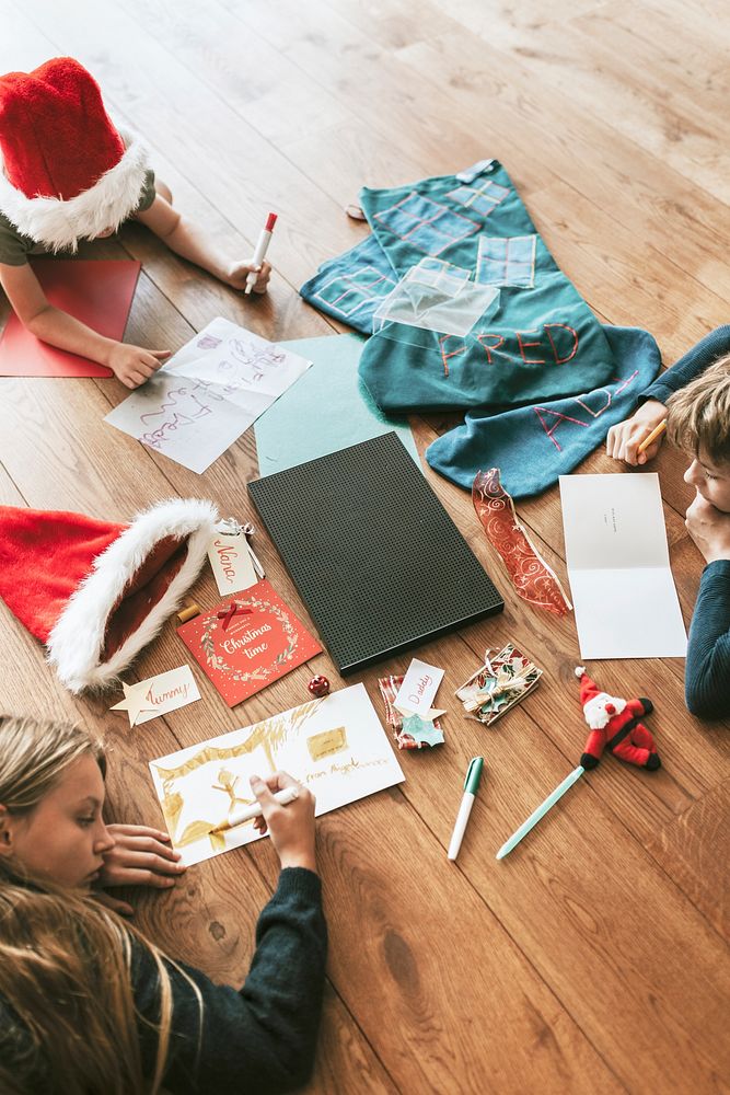 Kids writing Christmas cards on wooden floor