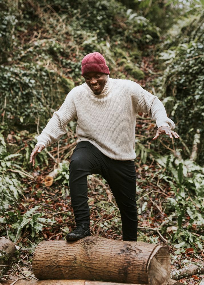 Black man in beige turtleneck sweater crossing log in autumn woods