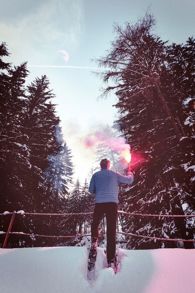 Man with snowblades holding a flare in the woods