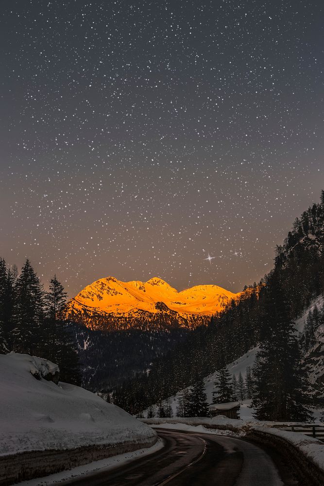 Sunlight on a snowed mountain top under a starry sky