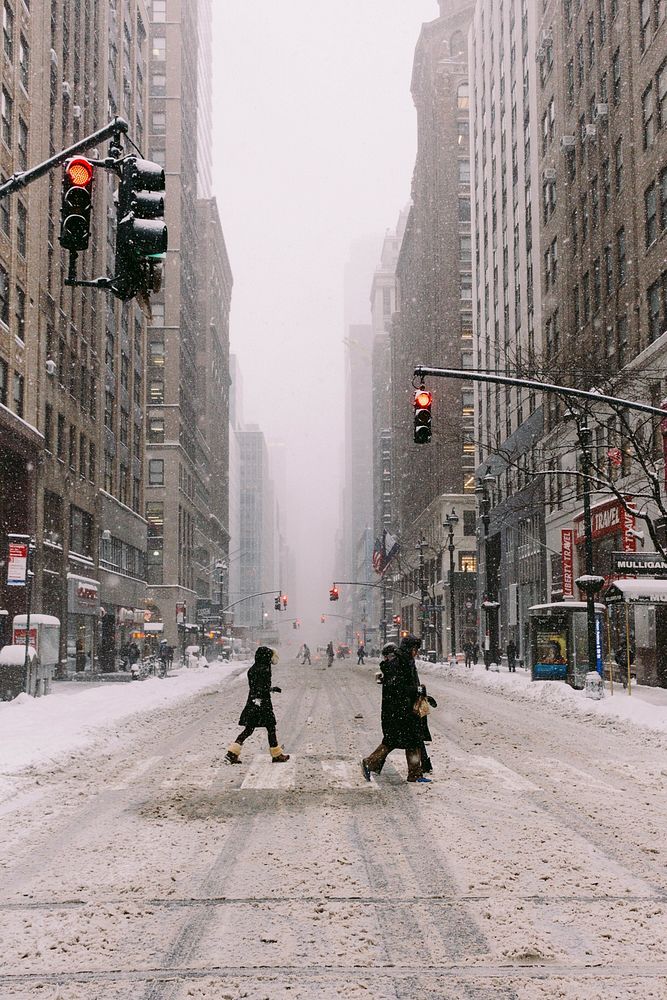 Crossing the city streets between tall buildings during a snowstorm on a cold winter day.